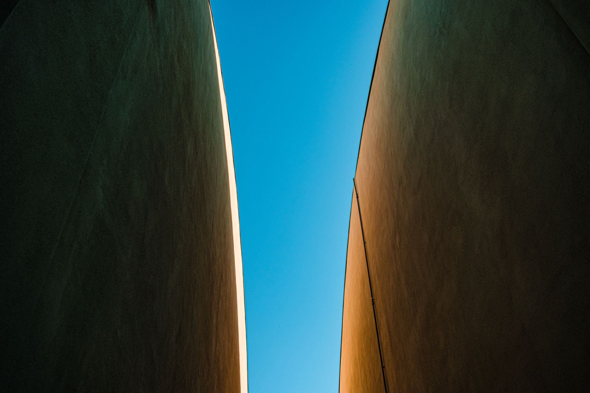 A minimalist perspective of a narrow gap between modern buildings under a bright blue sky.